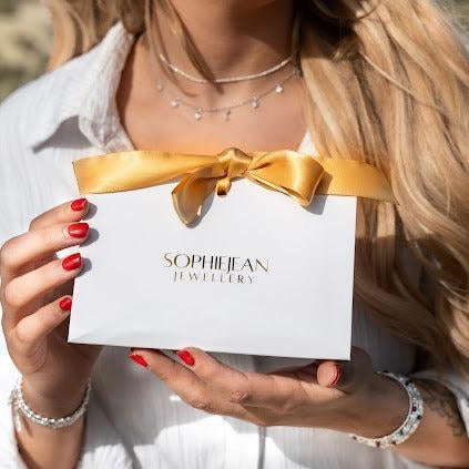 Person holding a white box with a gold bow and 'Sophie Jean Jewellery' branding.