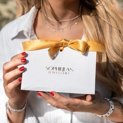 Person holding a white box with a gold bow and 'Sophie Jean Jewellery' branding.