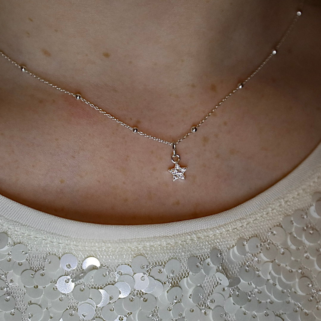 Necklace with a star pendant worn by a person, with a close-up on the necklace and skin.
