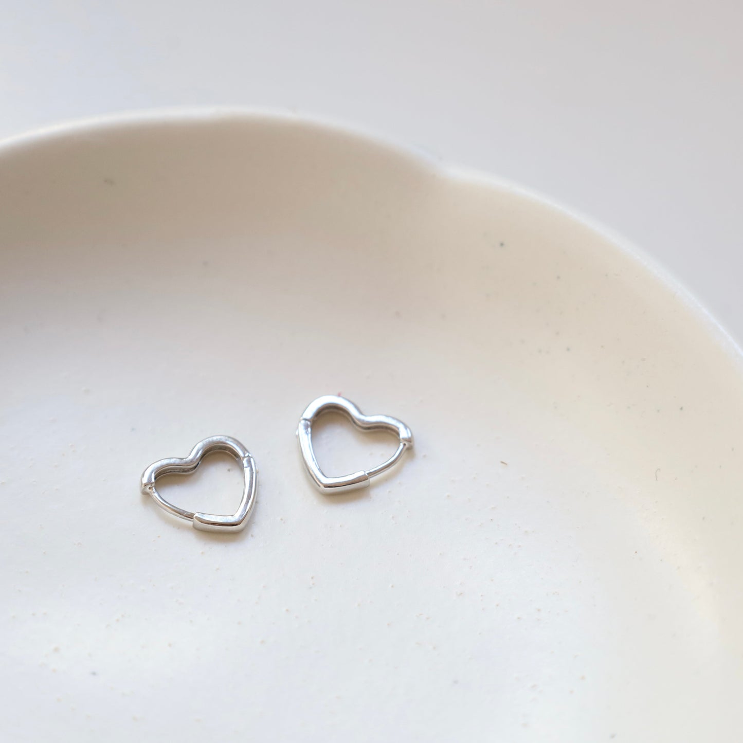 Silver heart-shaped earrings on a white ceramic plate