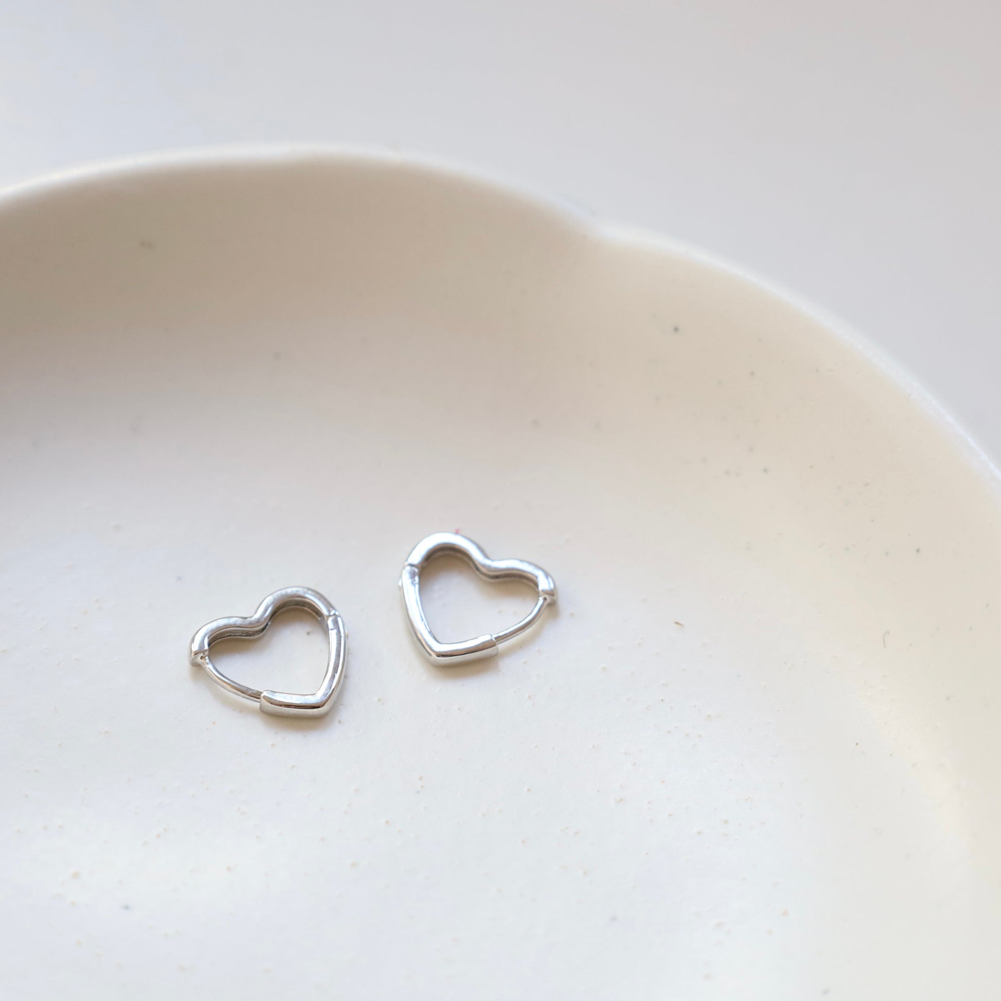 Silver heart-shaped earrings on a white ceramic plate