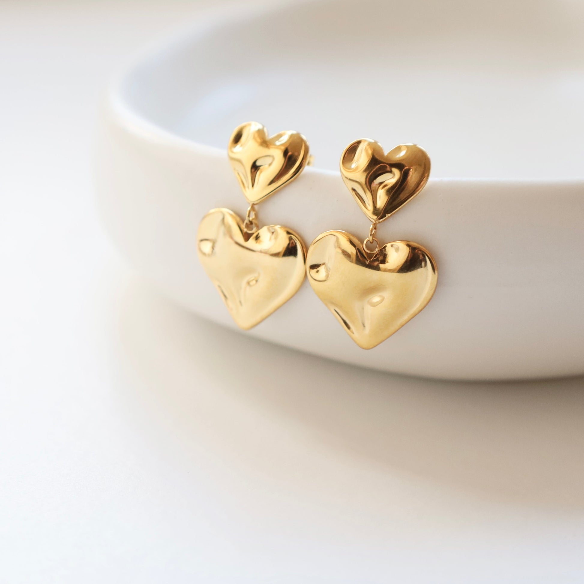 Gold heart-shaped earrings on a white dish
