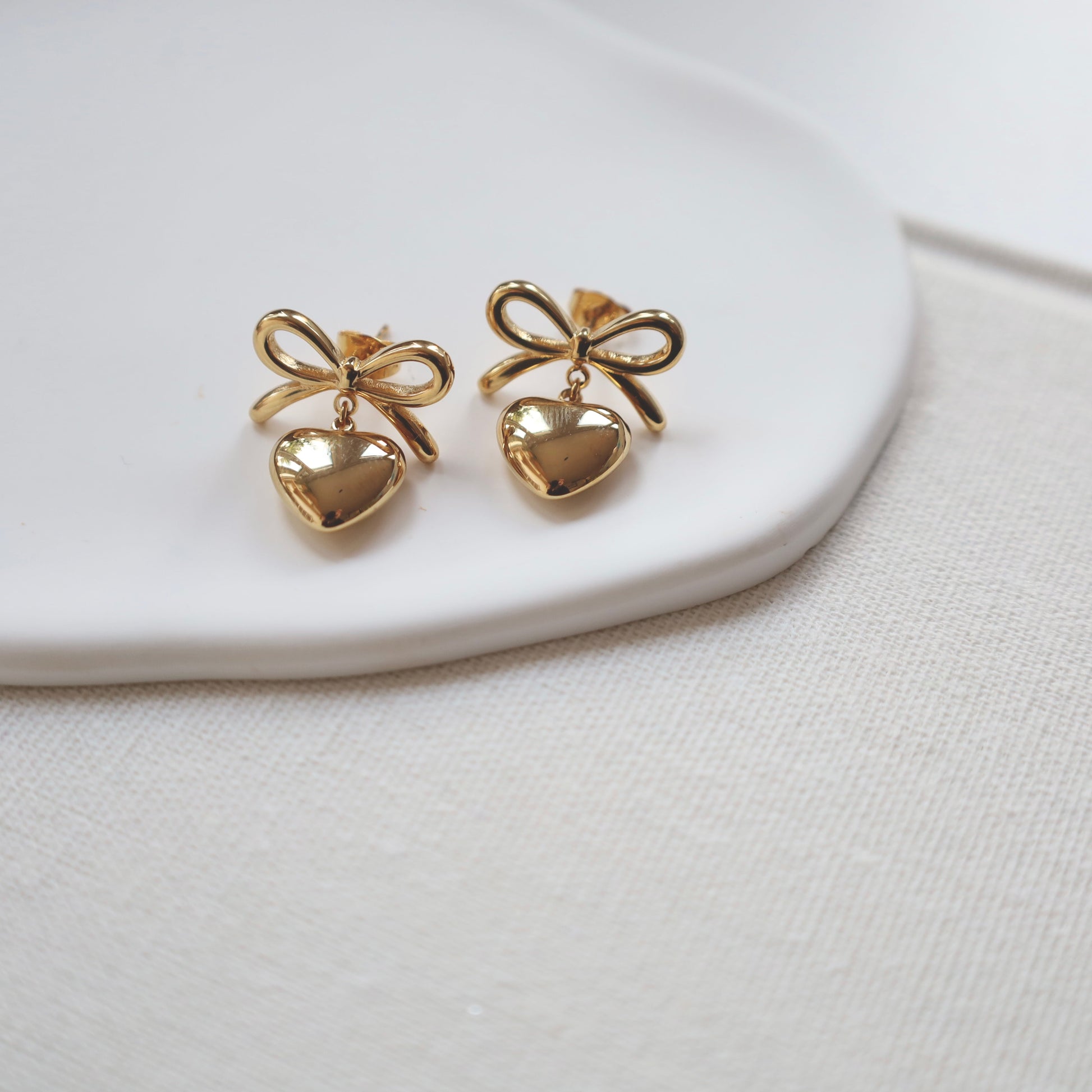 Gold bow-shaped earrings on a white ceramic plate with a white background