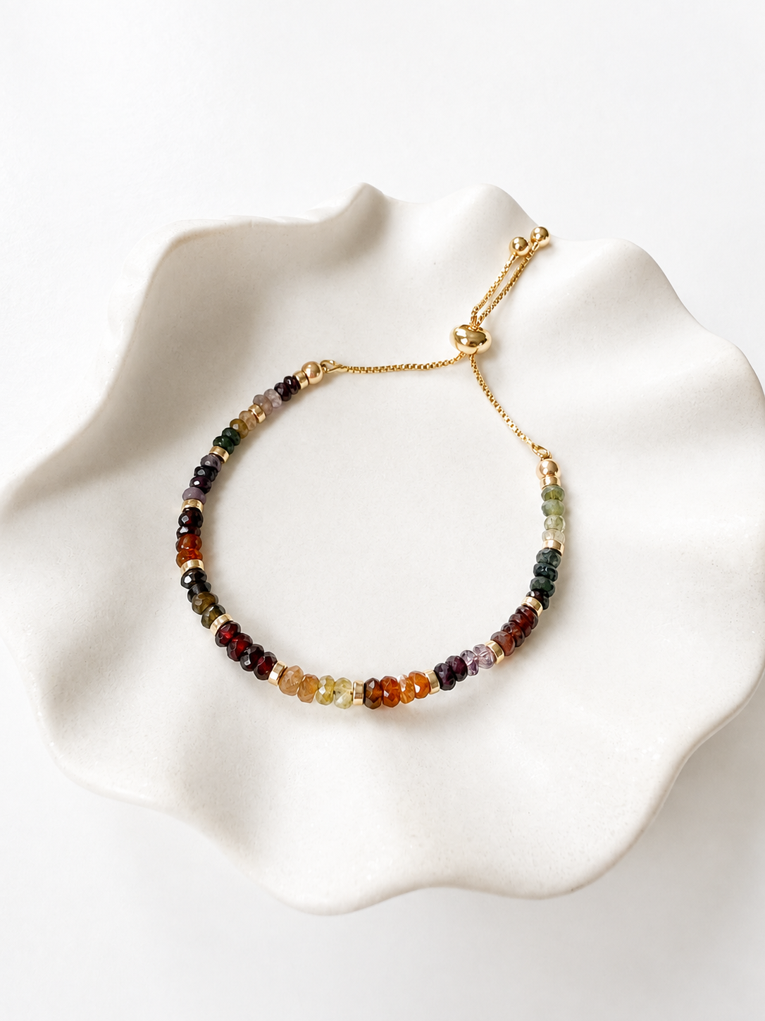 Adjustable gold Tundra Sapphire September birthstone bracelet on a white ceramic dish