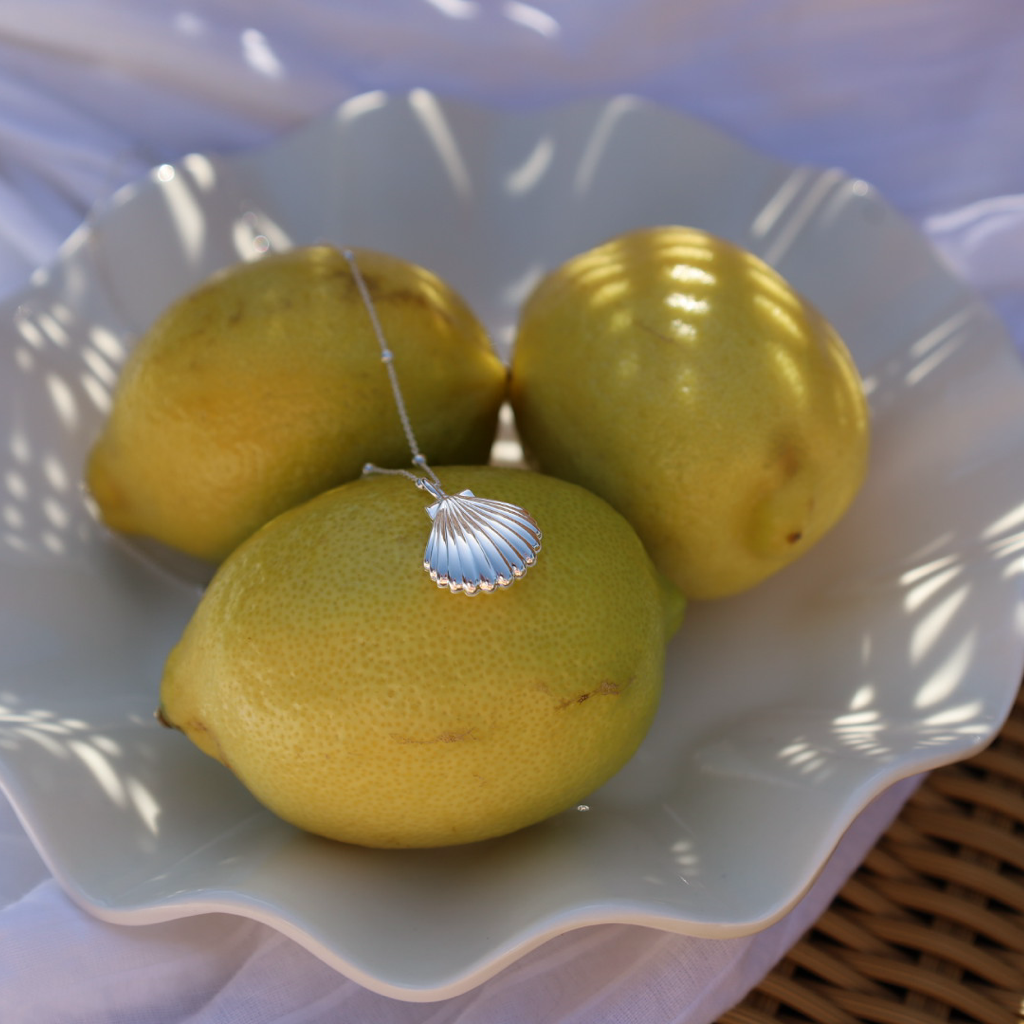 925 sterling silver shell locket necklace styled with fresh lemons on a ceramic dish.