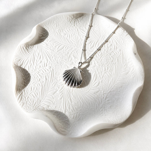 925 sterling silver shell locket necklace on a white textured ceramic dish.