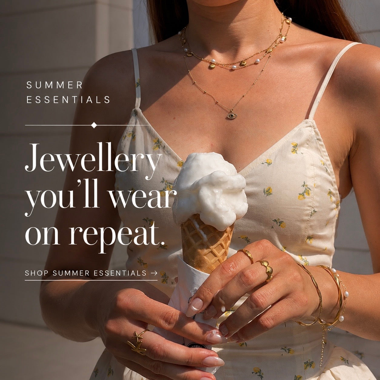 Woman wearing layered gold necklaces, bracelets and rings while holding an ice cream cone in the sunshine, showcasing the SophieJean Summer Essentials jewellery collection.